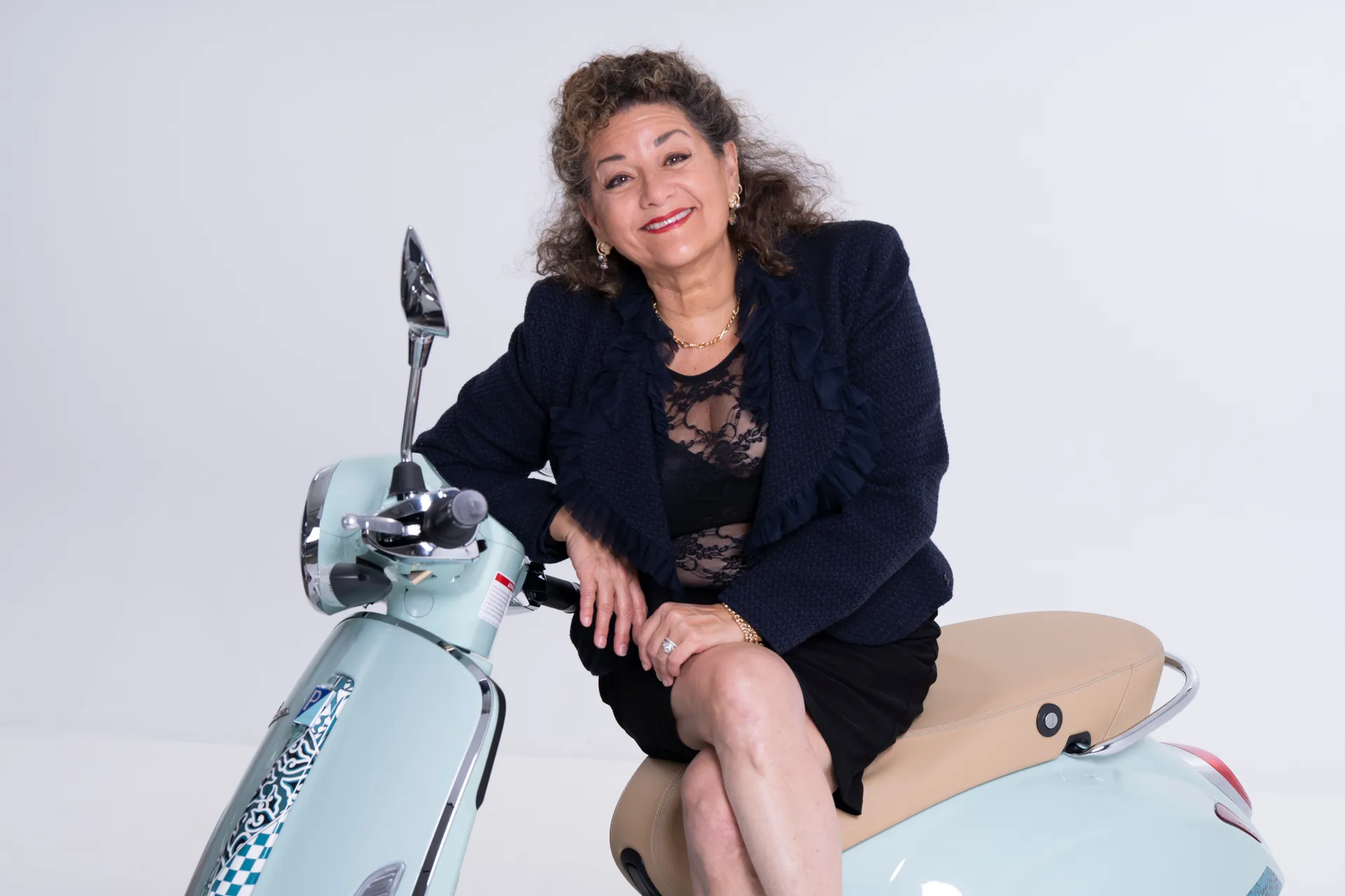 Sharon Azrieli seated on a mint-green Vespa scooter, studio portrait