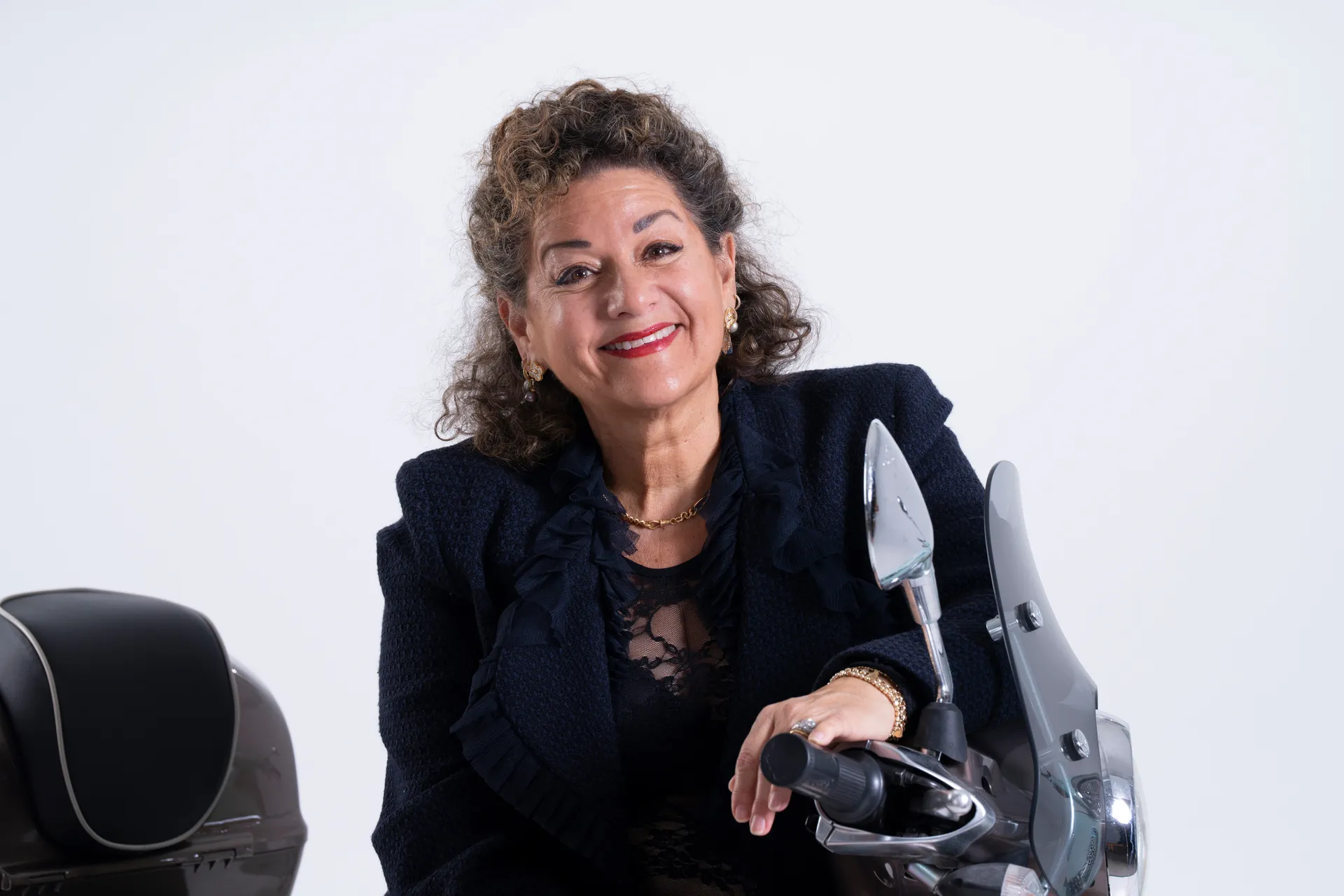 Sharon Azrieli leaning on a scooter, smiling, studio portrait