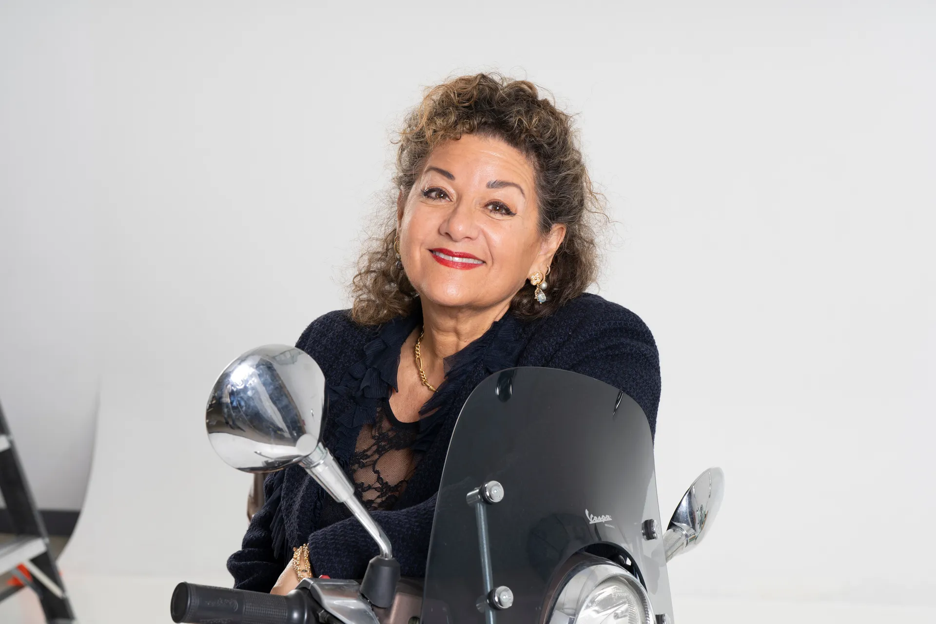Sharon Azrieli behind a Vespa windshield, close-up studio portrait